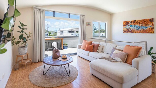 A spacious living room with a white sofa, a round coffee table, and a large window offering a view of a building and greenery outside. - Summer Sky - Oceanstays (Yamba)