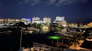 Una marina de noche con barcos amarrados, un paseo marítimo y edificios iluminados al fondo.
