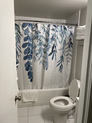 Ein Badezimmer mit Duschvorhang mit Blättermuster, Toilette und Handtuchhalter mit Handtüchern.