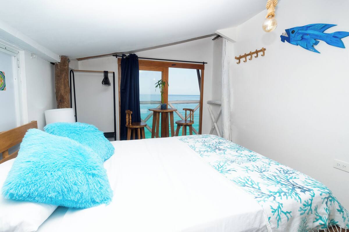 A bedroom with a bed, a view of the sea, and a balcony with a table and chairs.