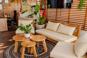 Sala de estar moderna com sofá, duas mesas redondas de madeira e plantas em vasos.