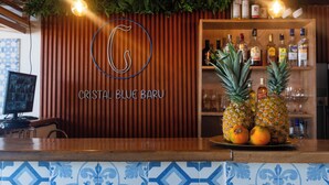 A bar area with a wooden counter, a sign reading "CRISTAL BLUE BARU", and a shelf with bottles and glasses. - Cristal Blue Baru (Cartagena)