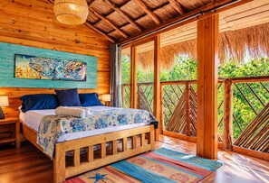 A wooden room with a bed, a painting, and a view of greenery. - Cristal Blue Baru (Cartagena)