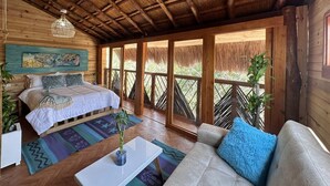 A room with a bed, a sofa, a coffee table, and a large window with a view of greenery. - Cristal Blue Baru (Cartagena)