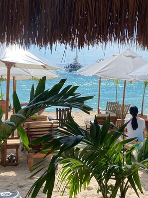 A beachside seating area with wooden chairs and umbrellas, overlooking the sea. - Cristal Blue Baru (Cartagena)