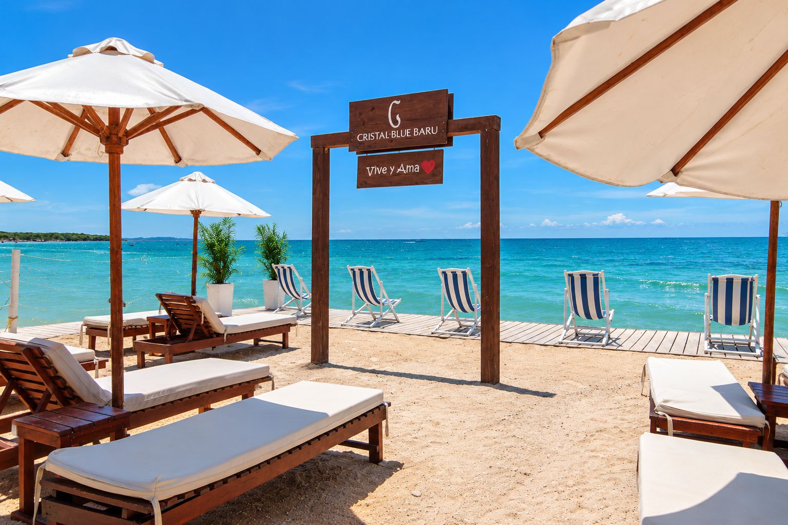 A beachside lounge area with wooden lounge chairs and white umbrellas, a wooden sign with 'Cristal Blue Baru' and 'Vive Ya Ama' written on it, and a view of the ocean.