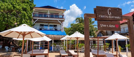 A beachside resort with lounge chairs and umbrellas, a sign for 'Cristal Blue Baru', and a building with a blue roof.