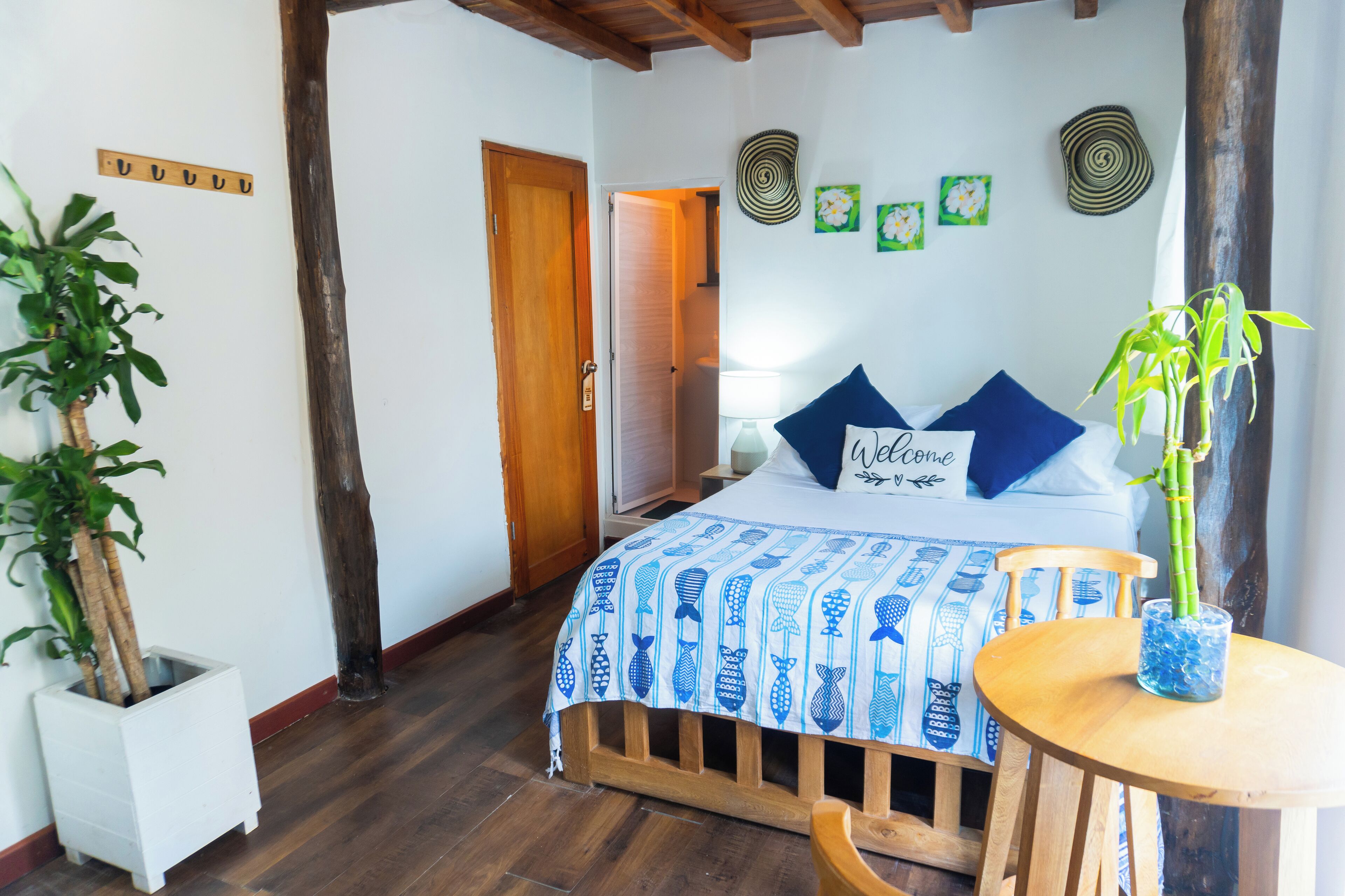 A bedroom with a bed, a bedside table, a chair, a potted plant, and a wooden floor.