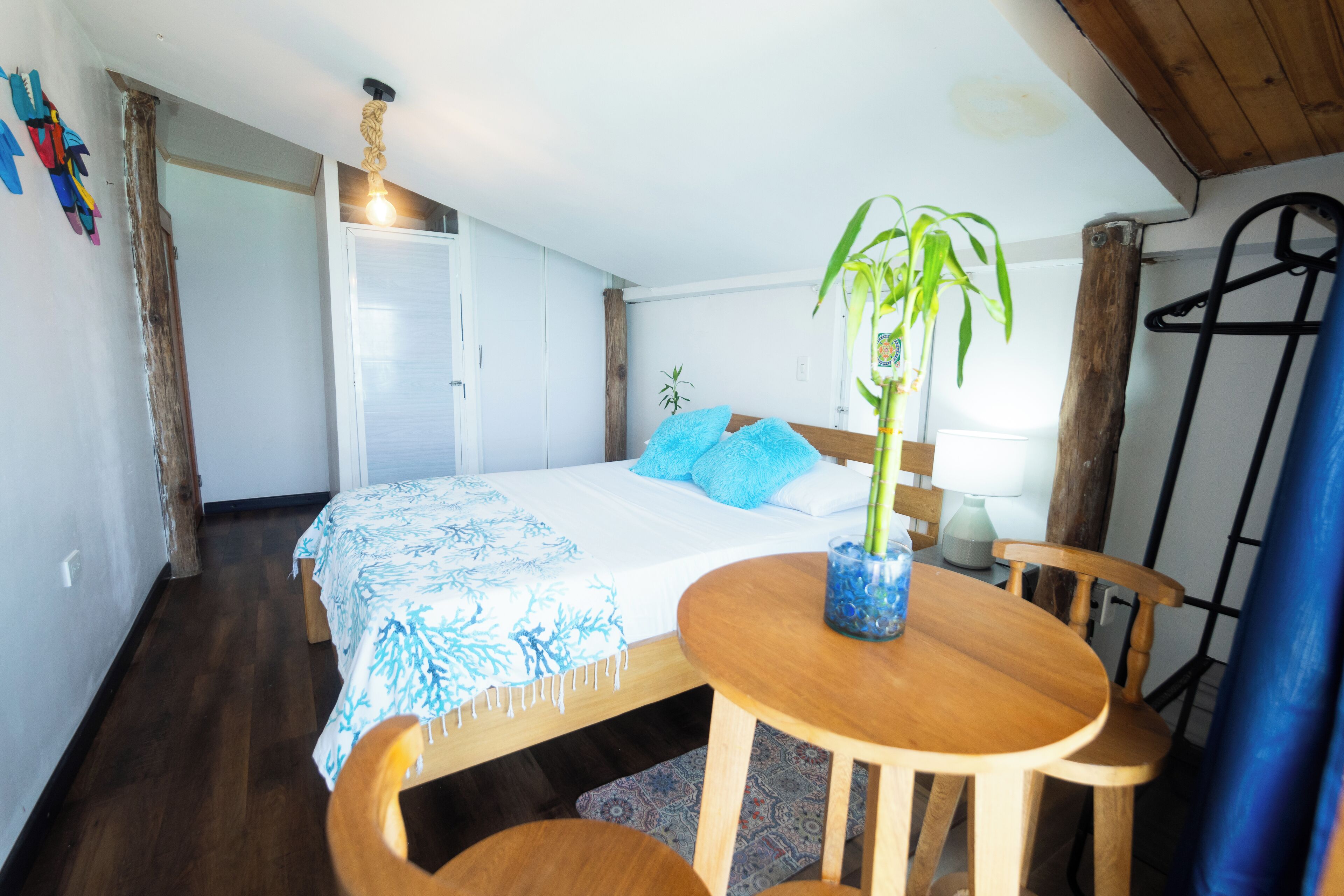 A bedroom with a bed, a bedside table with a plant, a wooden chair, and a hanging light fixture.