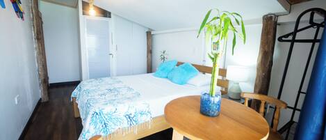 A bedroom with a bed, a bedside table with a plant, a wooden chair, and a hanging light fixture.