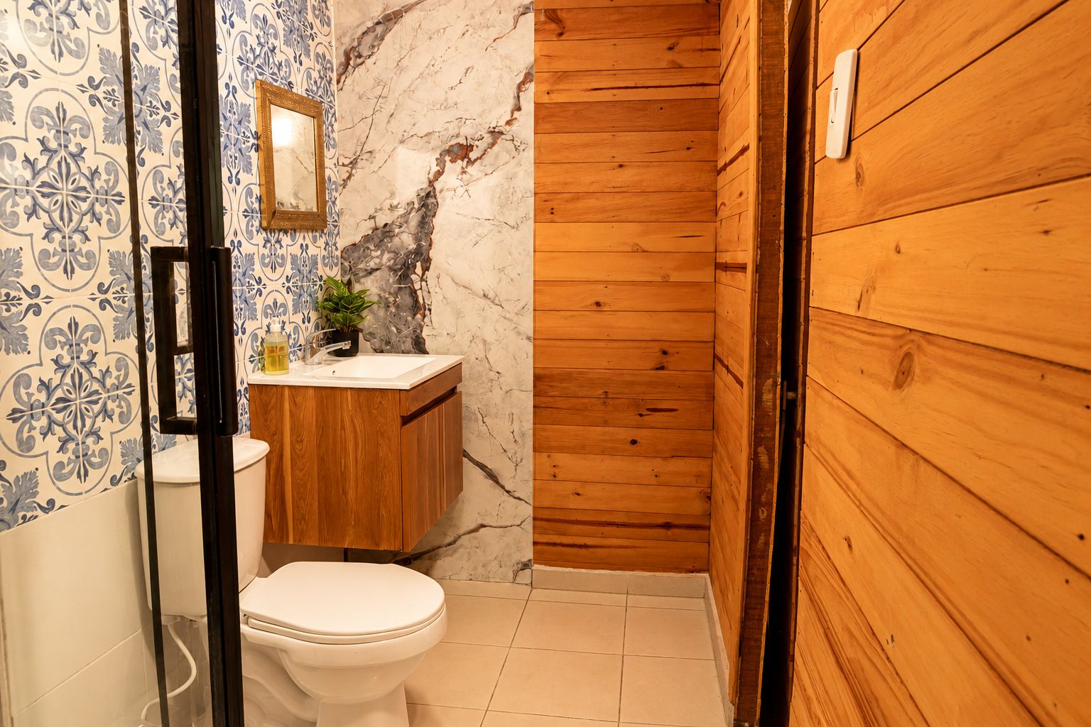 Een badkamer met een houten wastafelmeubel, een wit toilet en een marmeren wand.