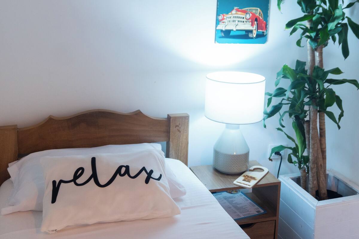 A bedroom with a bed, a nightstand, a lamp, a plant, and wall art.
