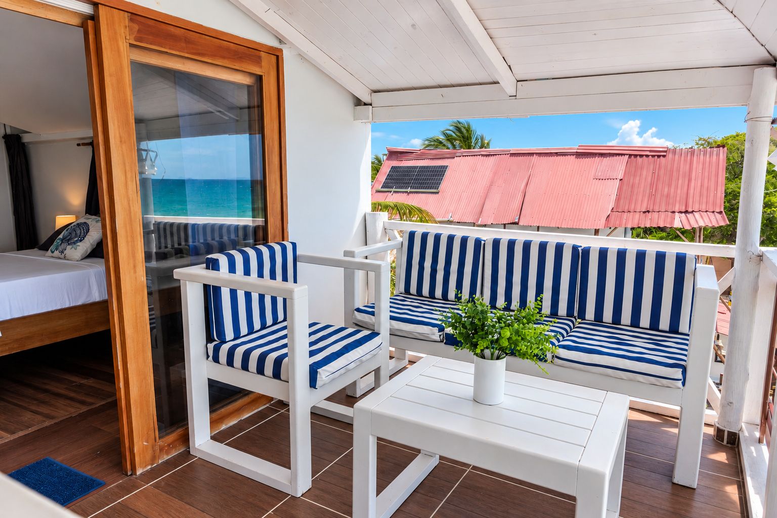 A room with a bed, a white sofa with blue stripes, a small table, and a view of the ocean.