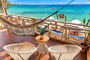 A wooden deck with a hammock, two wicker chairs, a small round table with a potted plant, and a view of the ocean with boats. - Cristal Blue Baru (Cartagena)