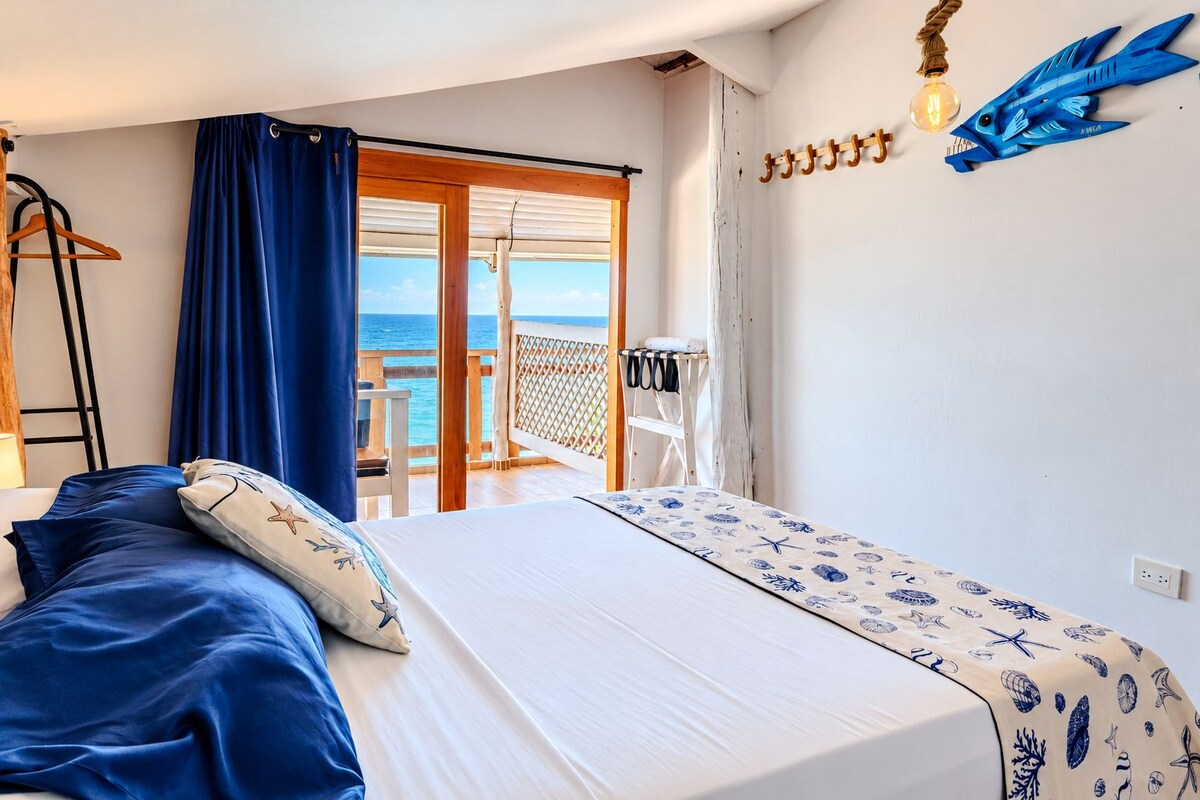 Ein Schlafzimmer mit Bett, Meerblick, einem Balkon und einer Wandleuchte.