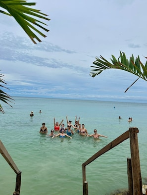 Eine Gruppe von Menschen in blauem Meer, manche stehen, manche schwimmen, mit einer Holzkonstruktion im Vordergrund.