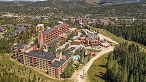 A large hotel complex with multiple buildings, surrounded by forested hills and mountains. - Cozy Ski-In/Out Studio In Building 4 | Kitchen | Hot Tubs, Dog Friendly (Breckenridge)