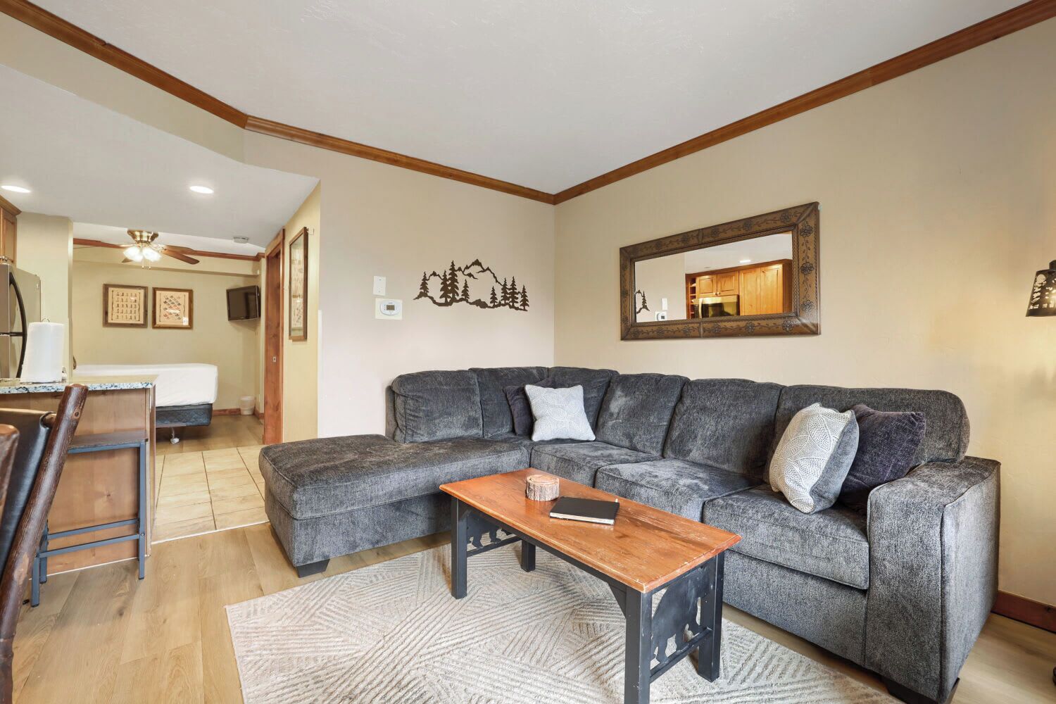 A living room with a sectional sofa, a wooden coffee table, and a kitchen in the background.