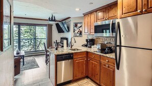A kitchen with wooden cabinets, stainless steel appliances, and a large window overlooking a deck. - Cozy Ski-In/Out Studio In Building 4 | Kitchen | Hot Tubs, Dog Friendly (Breckenridge)