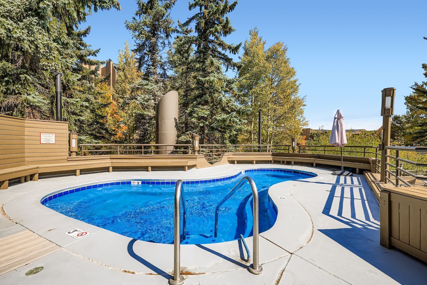 Una piscina con cubierta de madera, barandales metálicos y un cartel que indica prohibido bucear.