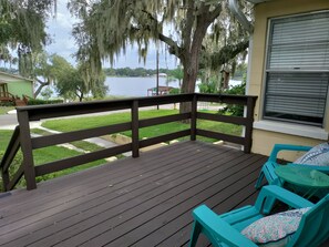 A wooden deck with a railing, turquoise chairs, and a view of a lake and distant buildings. - Romantic getaway, lakeview 5 min from the Downtown! (Clermont)