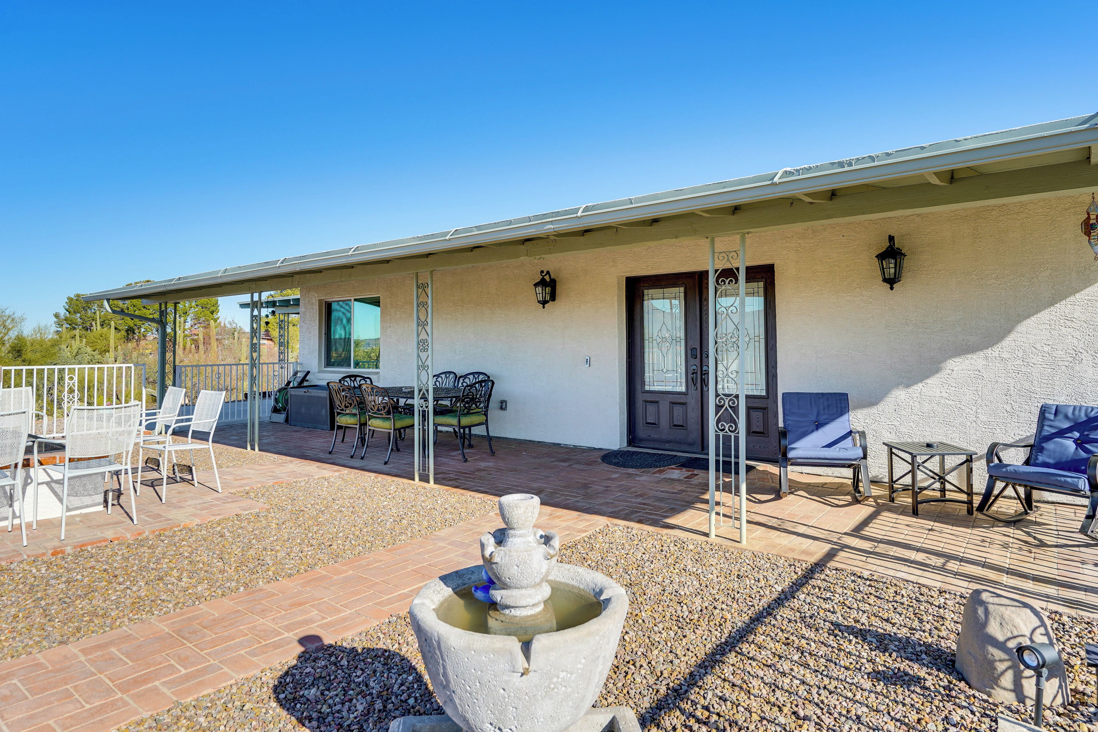 Un patio con mobiliario exterior, una fuente de piedra y un edificio con puerta y ventanas.