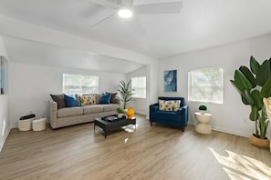 A spacious living room with a ceiling fan, two sofas, a coffee table, and large windows with blinds.