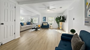 Ein geräumiges Wohnzimmer mit Deckenventilator, einem blauen Sofa, einem beigen Sofa und einem Couchtisch mit Dekoration.