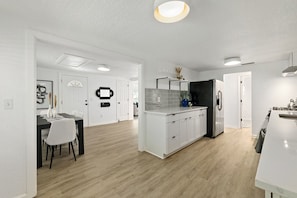 A modern kitchen with white cabinetry, a black refrigerator, and a dining area with a white table and chairs.