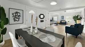 Ein modernes Wohnzimmer mit einem dunkelholzigen Esstisch, weißen Stühlen und einem blauen Sofa.