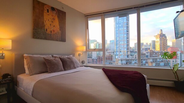 A hotel room with a large bed, a city view, a painting on the wall, and a TV mounted on the wall. - Charming Dwelling Downtown Vancouver (Vancouver)