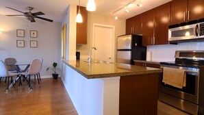A modern kitchen with a central island, stainless steel appliances, and a dining area with a ceiling fan and chairs. - Charming Dwelling Downtown Vancouver (Vancouver)