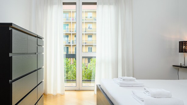 A hotel room with a bed, a dresser, and a view of a balcony with a building in the background.