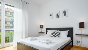 A modern bedroom with a large bed, white linens, and a view of a balcony.