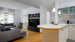 A modern kitchen with a central island, a built-in bookshelf, and a dining area with a grey sofa and a coffee table.