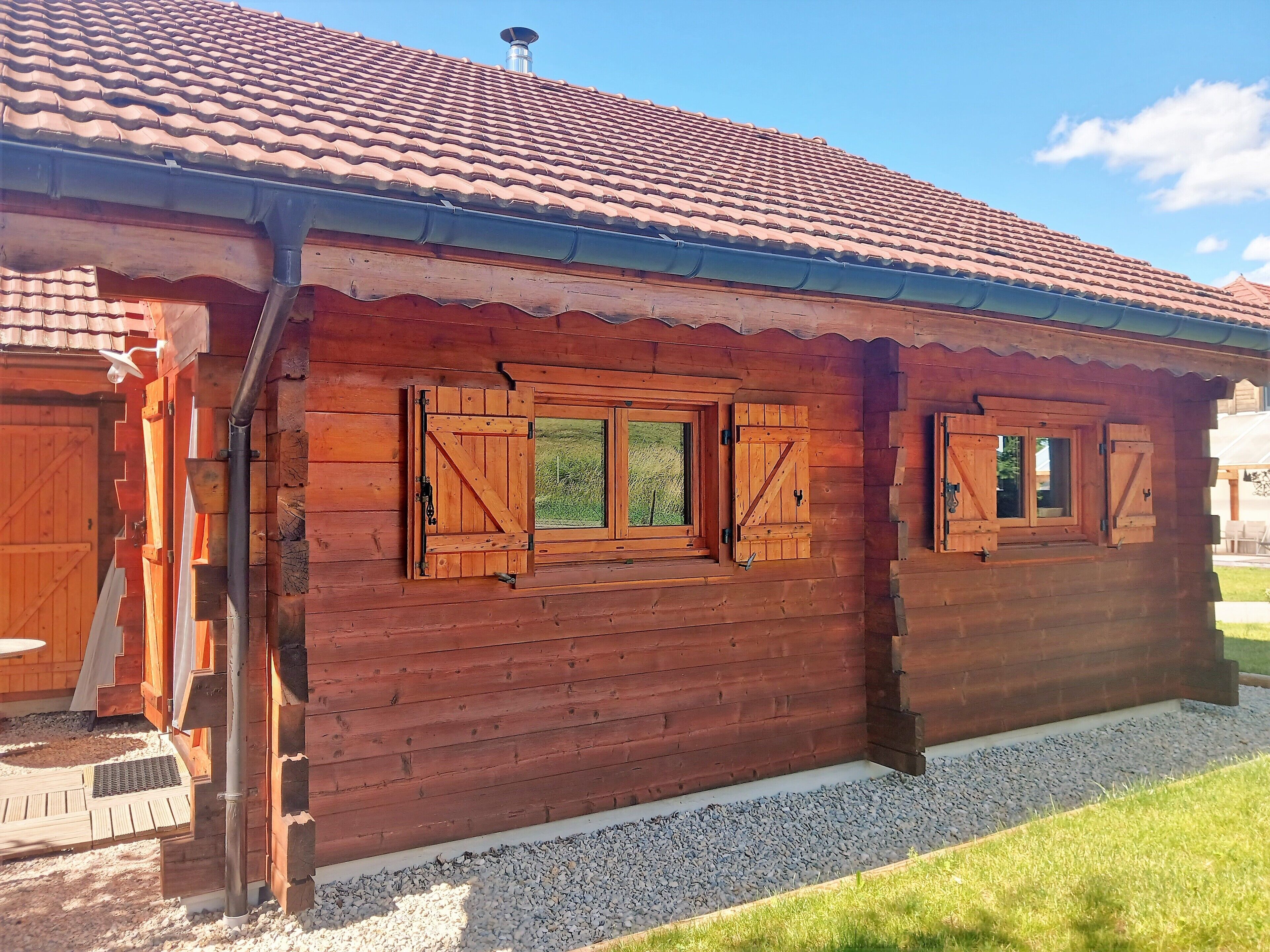 Una cabaña de madera con techo de tejas, contraventanas de madera en las ventanas y un camino de grava que conduce a la entrada.