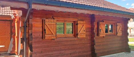 Una cabaña de madera con techo de tejas, contraventanas de madera en las ventanas y un camino de grava que conduce a la entrada.