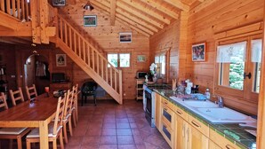 A wooden cabin interior with a dining area, kitchen, and a staircase leading to a loft. - Les 7 Coeurs, cosy chalet in Val Foncine (Foncine-le-Haut)