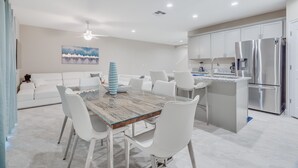 Een moderne keuken met roestvrijstalen apparatuur, een eethoek met een glazen tafel en witte stoelen, en een witte bank op de achtergrond.