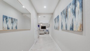 A modern hallway with white walls and a marble floor, leading to a living area with a TV and seating.
