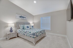 A bedroom with a bed, nightstand, lamp, and a wall-mounted TV.