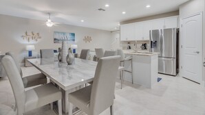 A modern kitchen with white cabinets, stainless steel appliances, and a marble dining table.