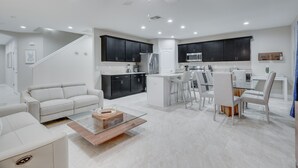 A modern kitchen with dark cabinets, a central island, and a dining area with white chairs.