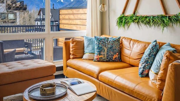 Een moderne woonkamer met een leren bank, een ronde salontafel en uitzicht op besneeuwde bergen door grote ramen.