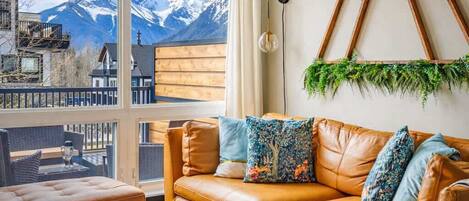 Un salon moderne avec un canapé en cuir, une table basse ronde et une vue sur des montagnes enneigées, visible à travers de grandes fenêtres.