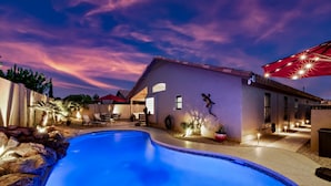 A swimming pool with a patio area, a house with a red awning, and a sunset sky. - Modern Southwest home w/heated pool oasis (Peoria)