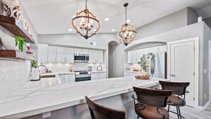 A modern kitchen with a large island, bar stools, and pendant lighting. - Modern Southwest home w/heated pool oasis (Peoria)