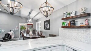 A modern kitchen with marble countertops, pendant lighting, and a dining area with a wooden table and chairs. - Modern Southwest home w/heated pool oasis (Peoria)