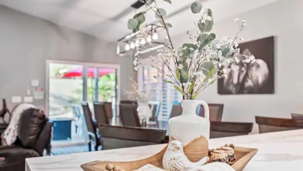 A dining area with a table set for two, featuring a vase with flowers, a wooden tray with eggs, and a pitcher. - Modern Southwest home w/heated pool oasis (Peoria)