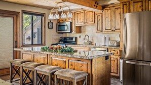 A kitchen with wooden cabinets, a stainless steel refrigerator, a microwave, and a large island with stools. - Amazing A Frame w/ Gorgeous Views of Bear Mountain + Spa (Big Bear Lake)